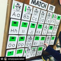 a young boy sitting in front of a wall covered with green and white cards that spell out the word match it