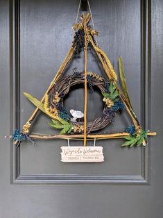 a triangle shaped wreath with leaves and flowers hanging on the front door to welcome guests