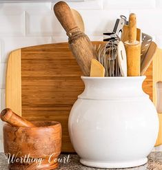 kitchen utensils in a white ceramic container next to a cutting board and knife holder