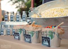 buckets filled with popcorn and candy are lined up on a table in front of a buffet