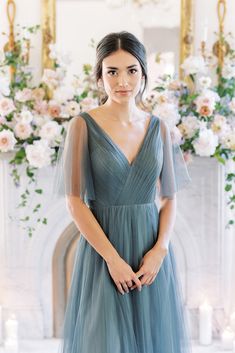 a woman standing in front of a fireplace wearing a blue dress and holding her hands on her hips