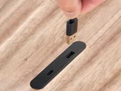 a hand is holding a usb stick and pressing it on the wooden surface with its thumb