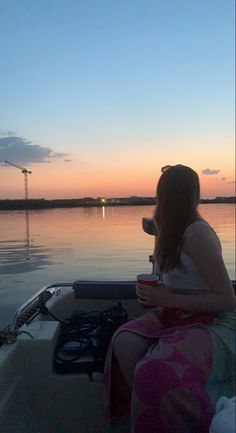 a woman sitting on the back of a boat at sunset drinking from a cup in her hand