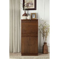 a tall wooden cabinet sitting next to a vase with flowers in it and a framed picture on the wall