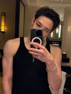 a man taking a selfie with his cell phone in a hotel room, wearing a black tank top