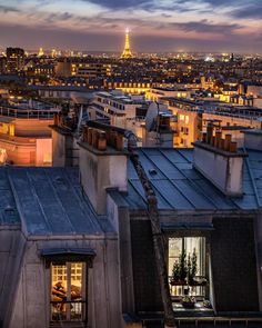 the eiffel tower is lit up in the distance from this rooftop top view