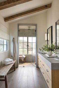 a large bathroom with wood floors and white walls, along with a wooden bench in the middle