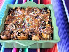 a green casserole dish filled with fruit and sprinkles on a colorful table cloth