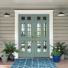 a blue front door with two potted plants on the side and an area rug