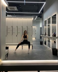 a woman is sitting on a bench in the middle of a room with lockers