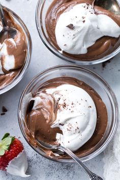 three bowls filled with chocolate pudding topped with whipped cream and strawberries on the side