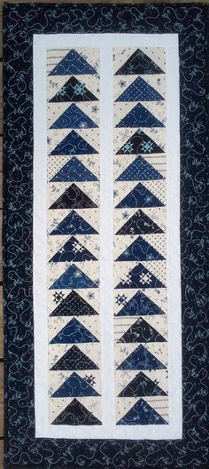 a quilted wall hanging with blue and white triangles on it's sides, in front of a wooden floor