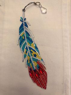 a beaded feather ornament is hanging on a white piece of cloth with beads