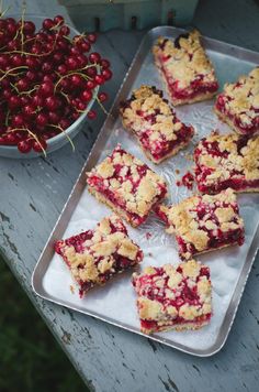 berry crumbler bars are on a tray next to a bowl of cherries