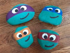 four painted rocks with faces on them sitting on a wooden floor in the shape of ninja turtles