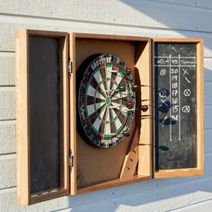 a dart and darts in a wooden box on the side of a building with chalk boards