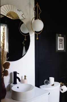 a white toilet sitting next to a bathroom sink under a round mirror on a wall