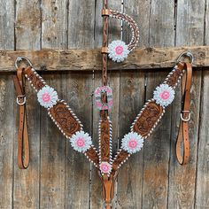 a brown and white horse bridle with pink flowers on the side, sitting against a wooden wall