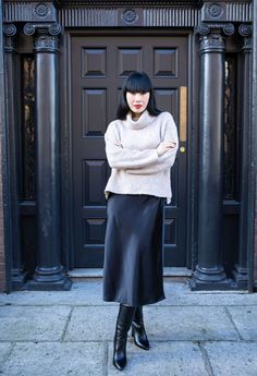 a woman standing in front of a black door wearing a white sweater and black leather skirt