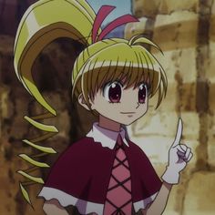 an anime character with blonde hair and big eyes pointing to something in her hand while standing next to a stone wall