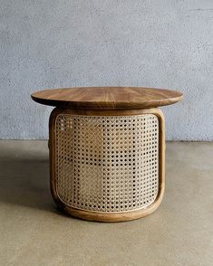 a round wooden table sitting on top of a cement floor next to a gray wall