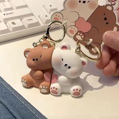 two key chains that are shaped like bears sitting on a desk next to a keyboard