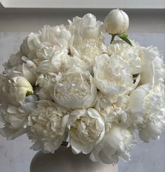 a vase filled with lots of white flowers on top of a marble table next to a window