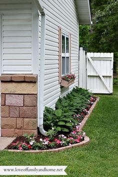 a flower bed in front of a house with flowers growing out of the planter