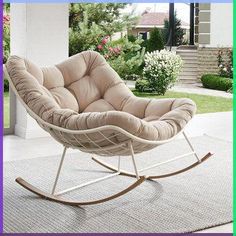 a white rocking chair sitting on top of a rug in front of a house with pink flowers