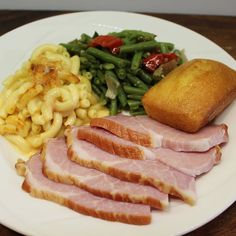 a white plate topped with ham, pasta and green beans next to a loaf of bread