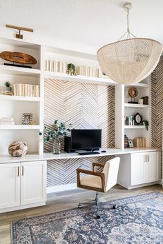 a home office with white cabinets and shelving units, an area rug and a hanging lamp