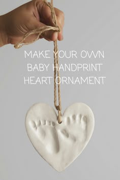 a hand holding a heart shaped ornament with the words make your own baby footprints on it