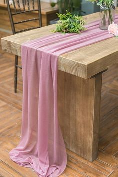 a wooden table topped with a vase filled with flowers next to a pink cloth draped over it