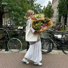 a woman is walking down the street with flowers in her hand and bicycles behind her