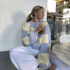 a woman sitting on a stool holding a cup in her hand and looking at the window