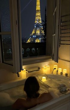 a woman in a bathtub with the eiffel tower lit up at night