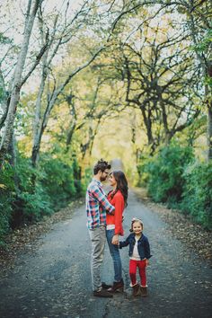 a man and woman holding hands while standing next to a small child on the side of a road