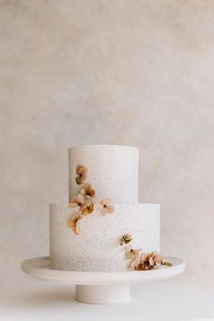 a three tiered white cake with flowers on the top and bottom, sitting on a plate