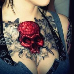 a woman with tattoos on her chest holding a red skull