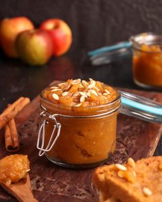 a glass jar filled with food sitting on top of a wooden cutting board next to apples and cinnamon sticks