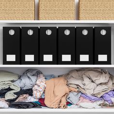 a white shelf filled with lots of clothes next to two bins full of shirts