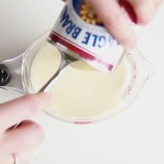 a person is pouring something into a glass container with a spoon in it and the other hand is holding a bottle