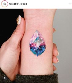 a woman's arm with a colorful diamond tattoo on her left wrist and the other hand behind her