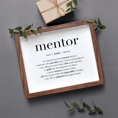 a wooden frame with the words mentor on it next to a present box and green leaves