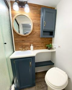 a white toilet sitting next to a bathroom sink under a wooden mirror mounted above it