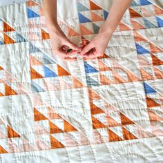 someone is making a quilt with their hands on top of the quilt, which has been made into a triangle pattern