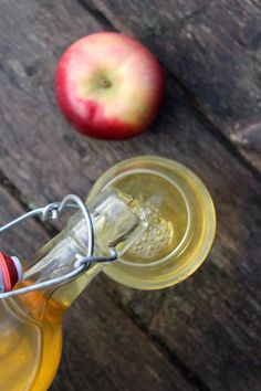 an apple sitting on top of a wooden table next to a glass jar filled with liquid