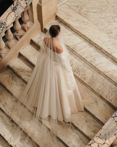 a woman in a wedding dress walking up some stairs with her veil over her head