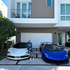 a man standing next to two sports cars in front of a house with balconies