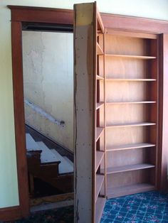 an open bookcase in the corner of a room with blue carpet and peeling paint on the walls